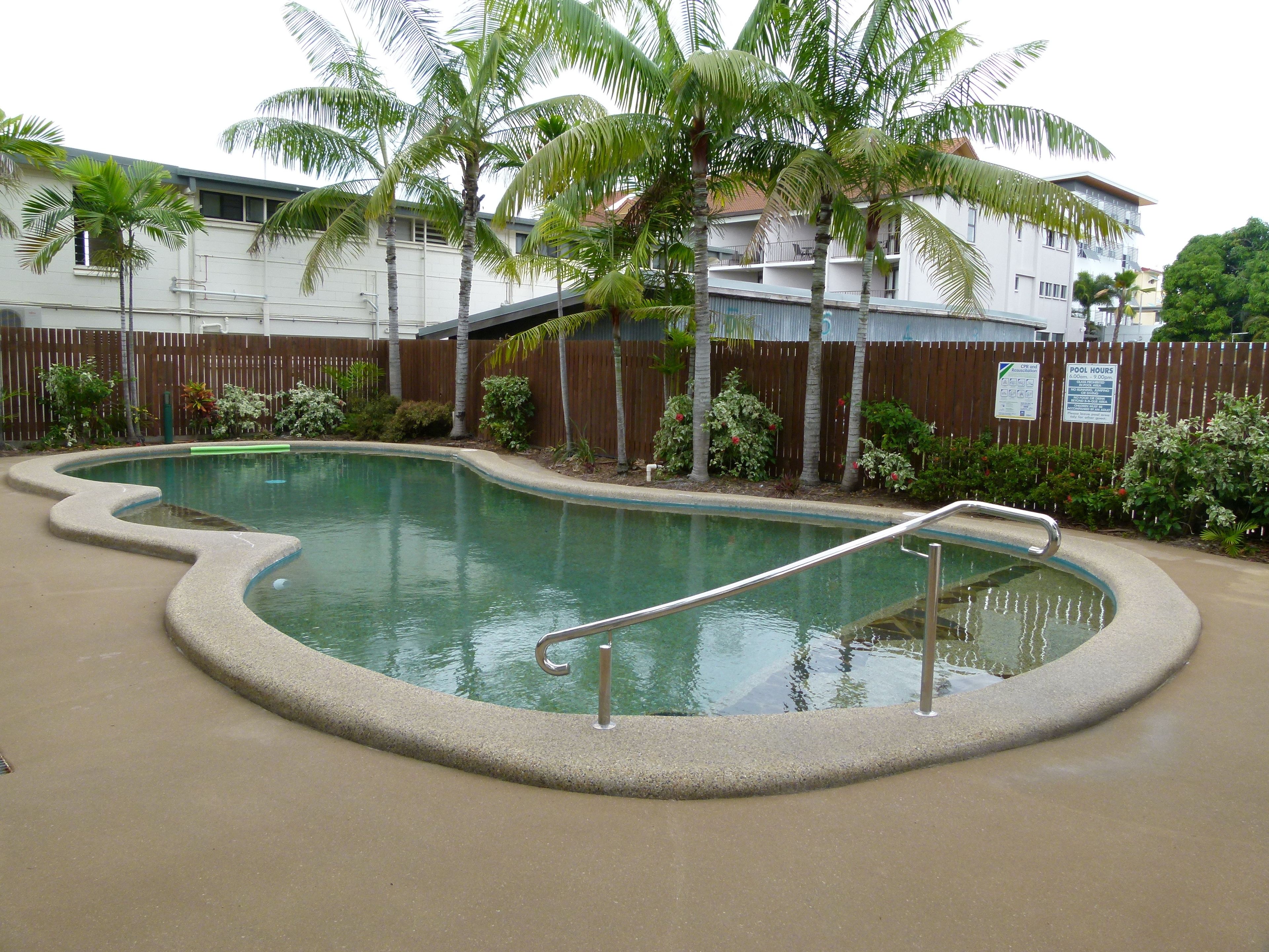 A swimming pool with a curved edge, surrounded by a wooden fence and palm trees.