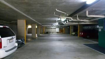 A multi-level parking garage with concrete pillars, overhead pipes, and several parked cars.