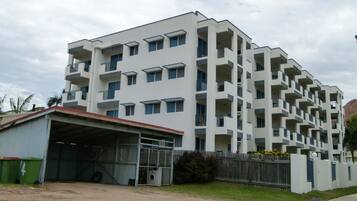 A multi-story residential building with a flat roof, multiple balconies, and a covered parking area.