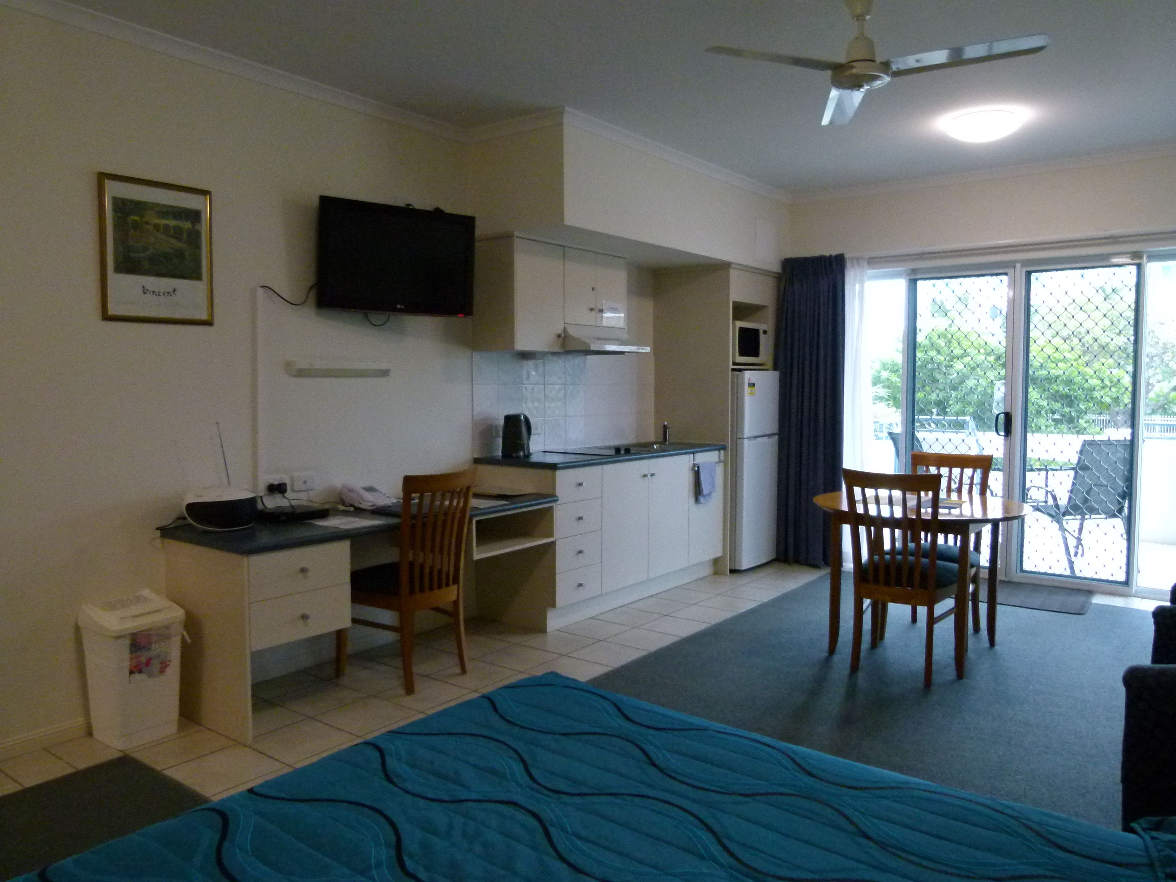 A compact hotel room with a kitchenette, a dining area, and a bed.