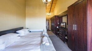 A hotel room with two beds, a desk with a chair, a wardrobe, and a chandelier.