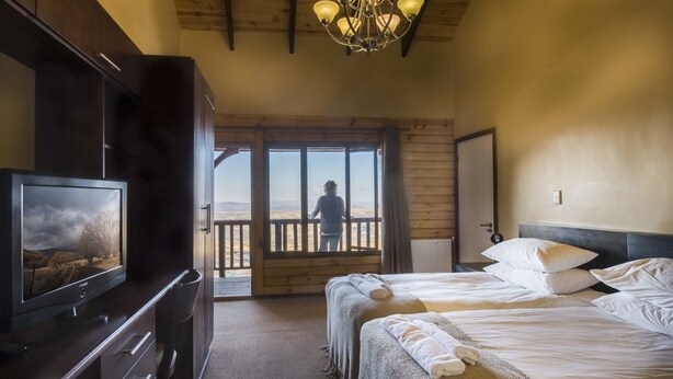 A hotel room with a large bed, a TV, and a balcony with a view of the mountains.