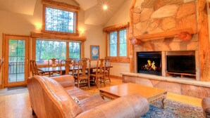 A cozy living room with a stone fireplace, wooden furniture, and large windows. - Spacious Frisco Cabin w/ Hot Tub, Sauna & Mountain Views—Minutes to Ski Resorts! (Frisco)