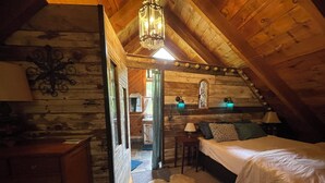 Un dormitorio acogedor en el ático con paredes de madera, techo inclinado, cama, mesita de noche y lámpara colgante.