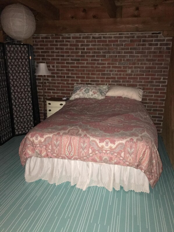 Une pièce avec un mur dont le motif imite des briques, un lit recouvert d’une couvre-lit à motifs, une table de chevet, une lampe et un rideau à motifs.