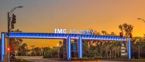 An IMG Academy entrance with a blue illuminated archway, a pedestrian crossing, and traffic lights.