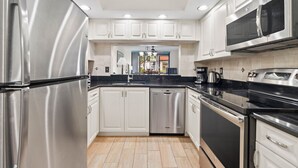 Una cocina moderna con electrodomésticos de acero inoxidable, armarios blancos y una encimera negra.