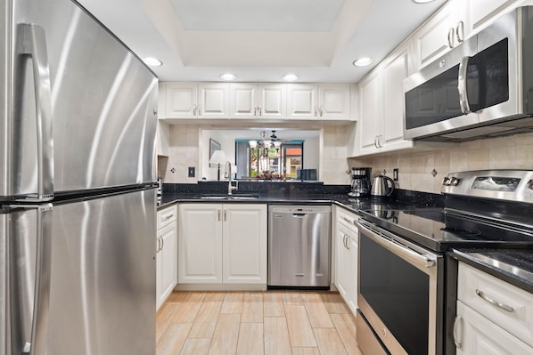 A modern kitchen with stainless steel appliances, white cabinetry, and a black countertop. - *Villa Bella* Executive 2BR Condo w/2 Pools, Mins to IMG/Beach/Anna Maria Isl (Bradenton)