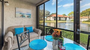 Una habitación con sofá color beige, un cuadro y vista a un lago con edificios al fondo.