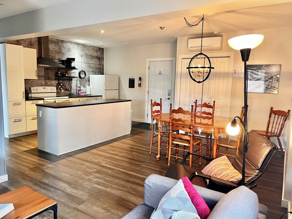 A modern kitchen with white cabinets, a central island, and a dining area with wooden chairs and a glass table.