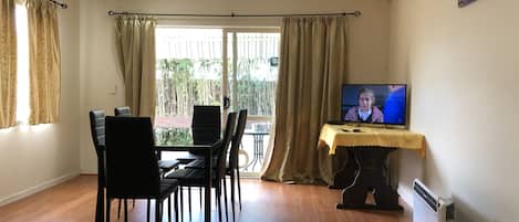 A room with a dining table, chairs, a television, and a radiator.