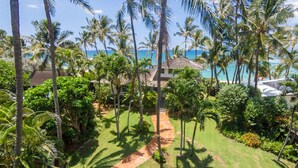 Een tropisch resort met een verzorgde tuin, palmbomen en uitzicht op de oceaan.