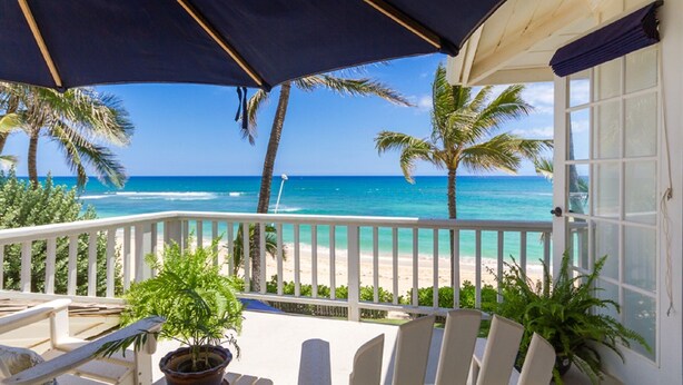 Een balkon met uitzicht op de oceaan, palmbomen en een strand.