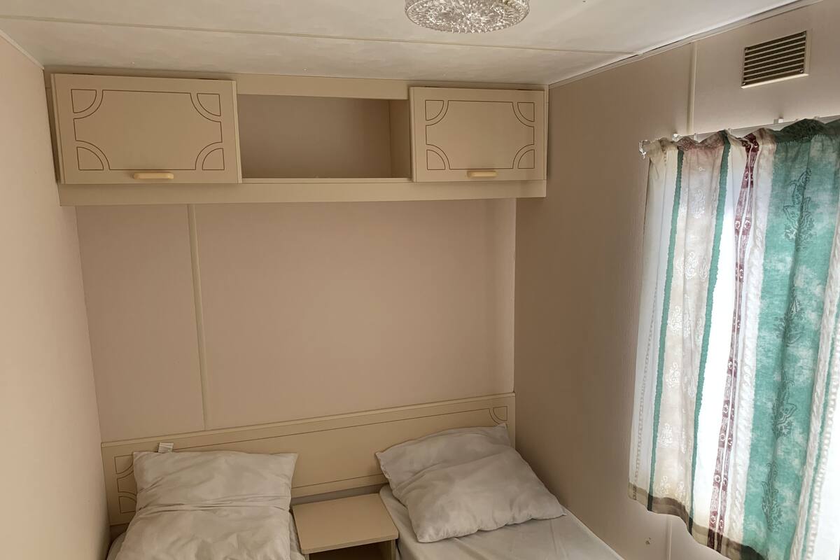Two single beds with matching headboards and footboards, each with a small shelf for storage, in a simple and functional room.