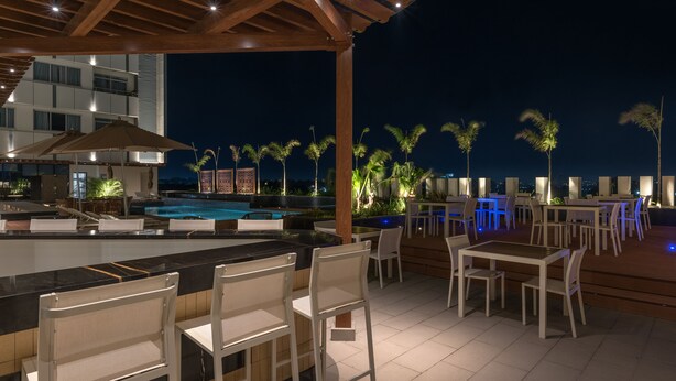An outdoor bar area with a pool, chairs, and tables under a wooden pergola at night. - Neelkanth Sarovar Premiere (Lusaka)
