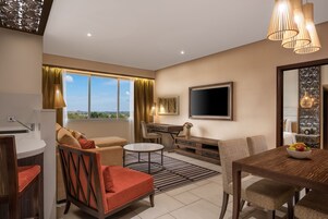 A modern living room with a sofa, armchair, dining table, and a TV.