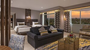 A modern hotel room with a large bed, a sofa, and a view of the cityscape at sunset. - Neelkanth Sarovar Premiere (Lusaka)