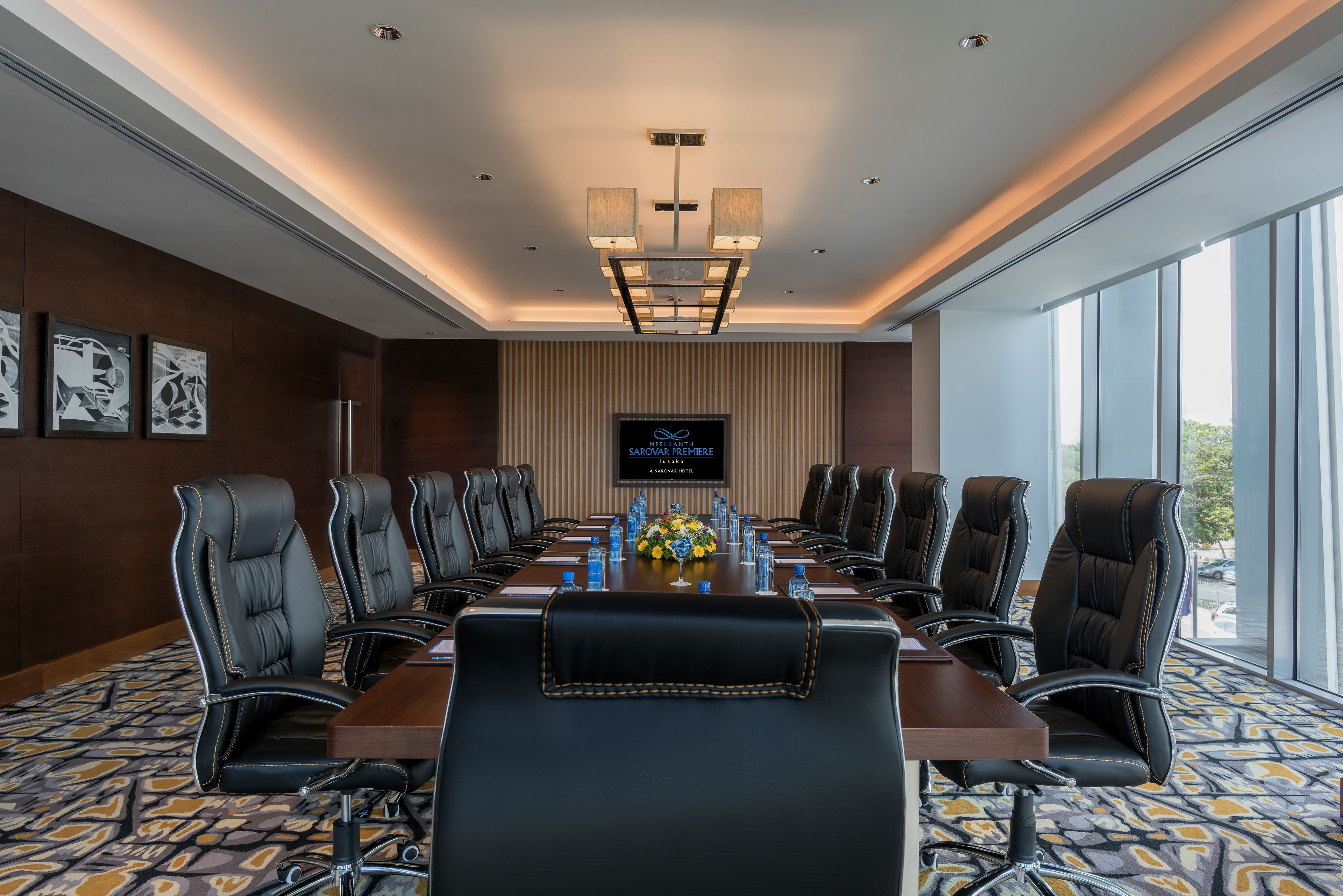 A conference room with a long table, multiple chairs, a television screen, and a large window.