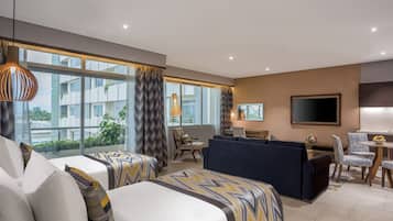 A hotel room with two beds, a sofa, a TV, and a dining area.