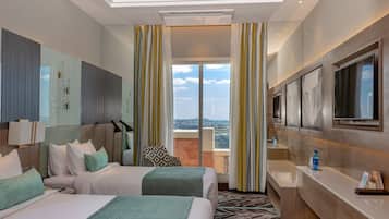 A hotel room with two beds, a large TV, a bathroom, and a balcony with curtains.