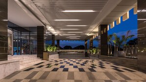 A spacious lobby with a checkered floor, modern lighting, and a view of palm trees at dusk. - Neelkanth Sarovar Premiere (Lusaka)