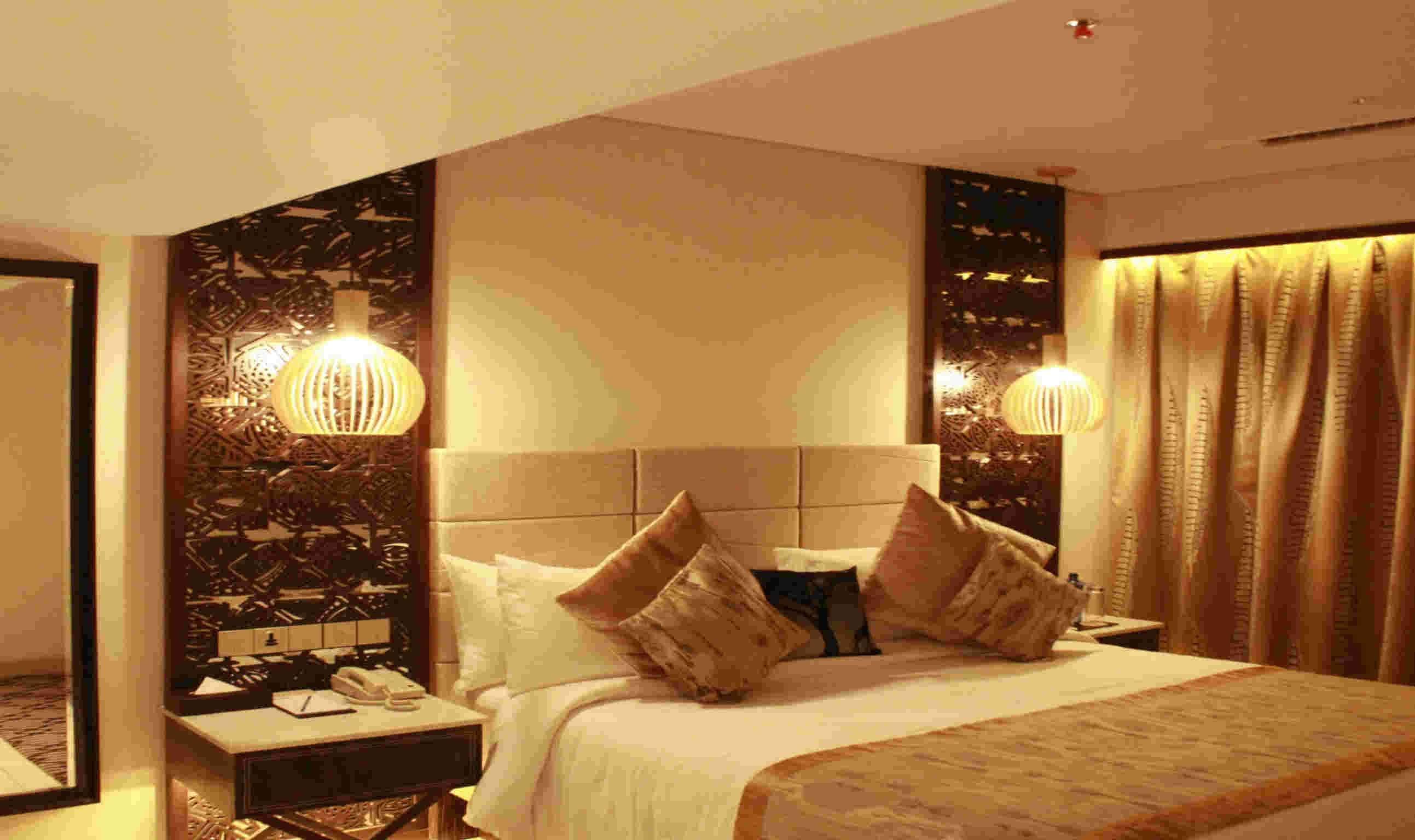 A hotel room with a large bed, two bedside tables, a nightstand, and a decorative wall panel.
