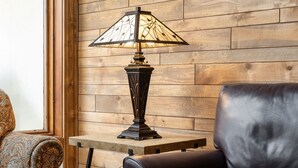 A living room with a wooden wall, a leather sofa, a patterned armchair, a table with books, and a floor lamp. - Montaneros 321 -1 Bedroom Platinum (Vail)