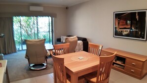 Un vaste espace de vie comprenant une table à manger en bois, des chaises et un canapé. Une grande fenêtre laisse entrer la lumière naturelle et offre une vue sur la verdure environnante.