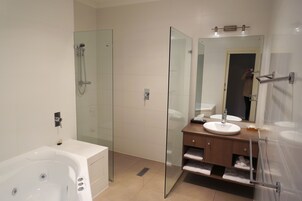 Un baño moderno con ducha envuelta en vidrio, bañera blanca y tocador de madera con lavabo.