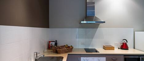 A modern kitchen with a stainless steel sink, a built-in oven, a microwave, and a stainless steel range hood. There are baskets on the counter and a red kettle.