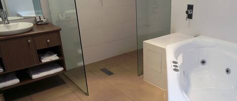 Un baño moderno con cabina de ducha de vidrio, una bañera blanca y un mueble de tocador de madera con toallas.