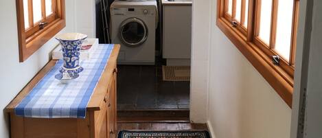 A narrow hallway with a washing machine, a drying rack, and a window with a view of greenery.