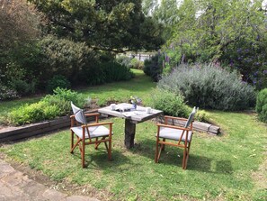 An outdoor seating area with two wooden chairs and a table, surrounded by lush greenery and flowering plants. - A Must At Coonawarra (Penola)