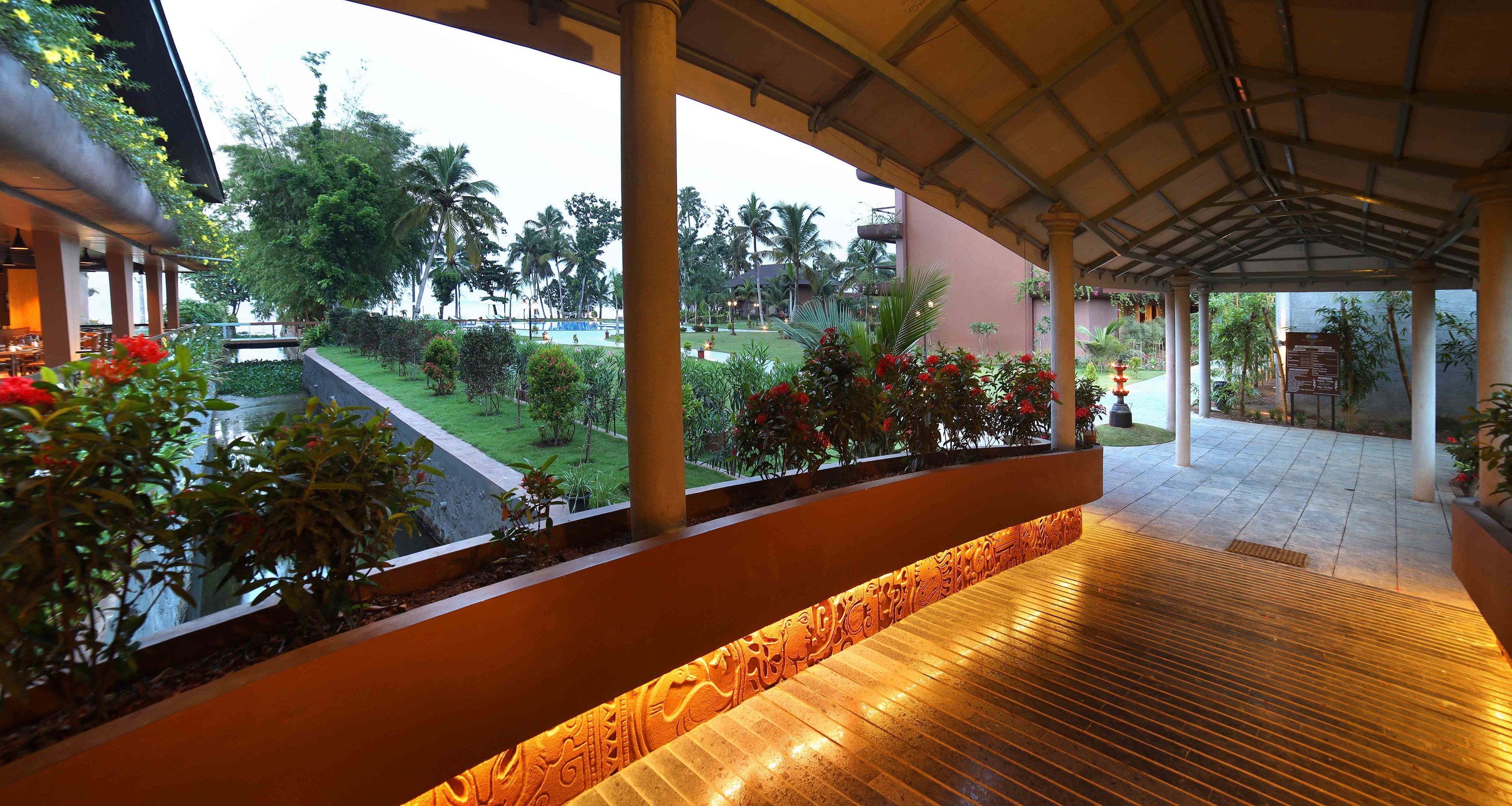 A covered outdoor area with a view of a pool and garden, featuring columns and potted plants.