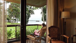 A room with a view of a lake, a wicker chair, a table with a tray, and a lamp. - Uday Backwater Resort (Ambalapuzha)