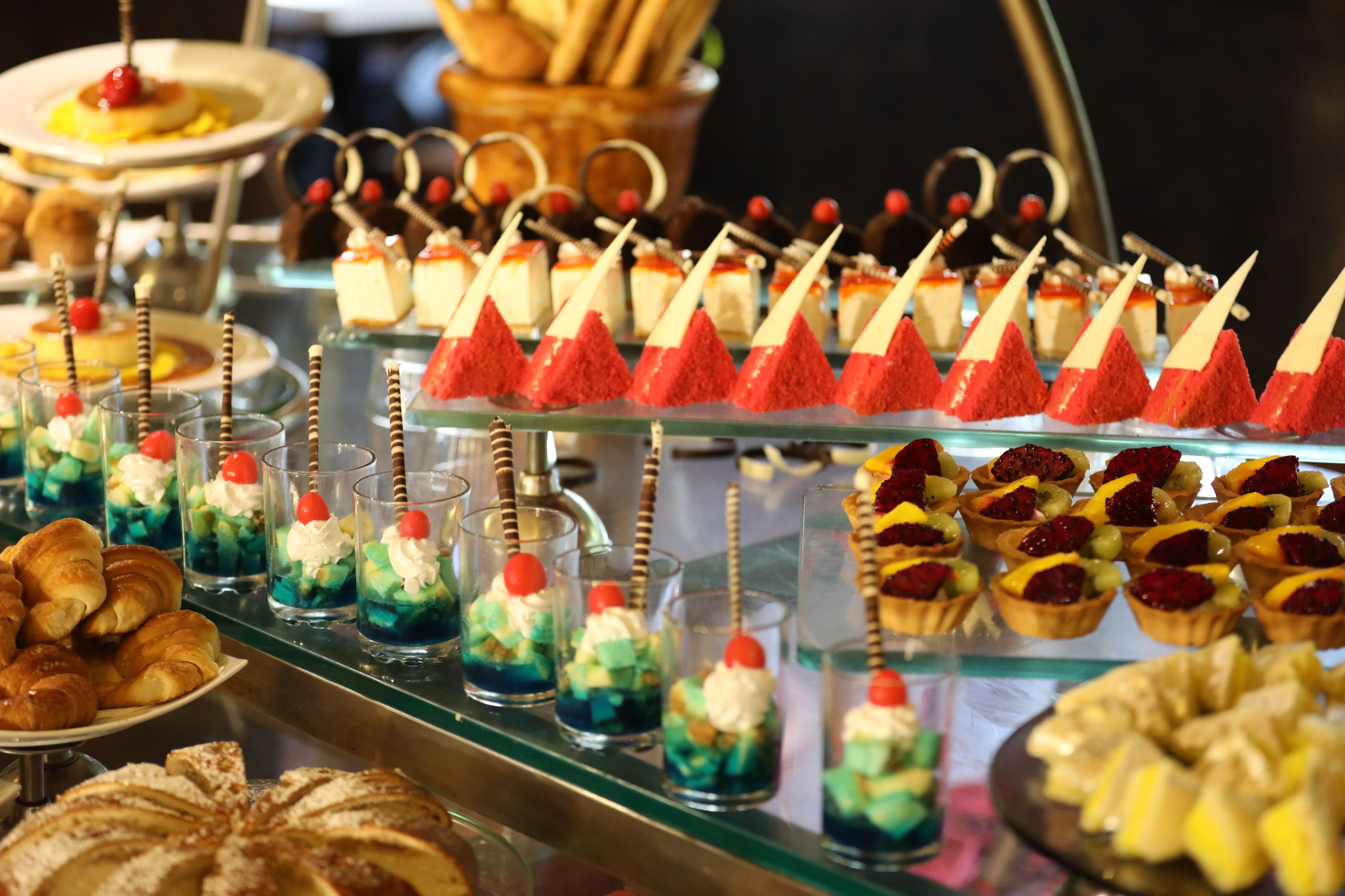 A buffet with various desserts and pastries, including mini cakes, tarts, and fruit arrangements.