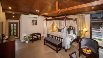 A four-poster bed with a canopy, a wooden bench, a dining table, and a seating area with a fruit basket.