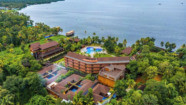 An aerial view of a resort with multiple buildings, a swimming pool, and lush greenery surrounding a large body of water. - Uday Backwater Resort (Ambalapuzha)