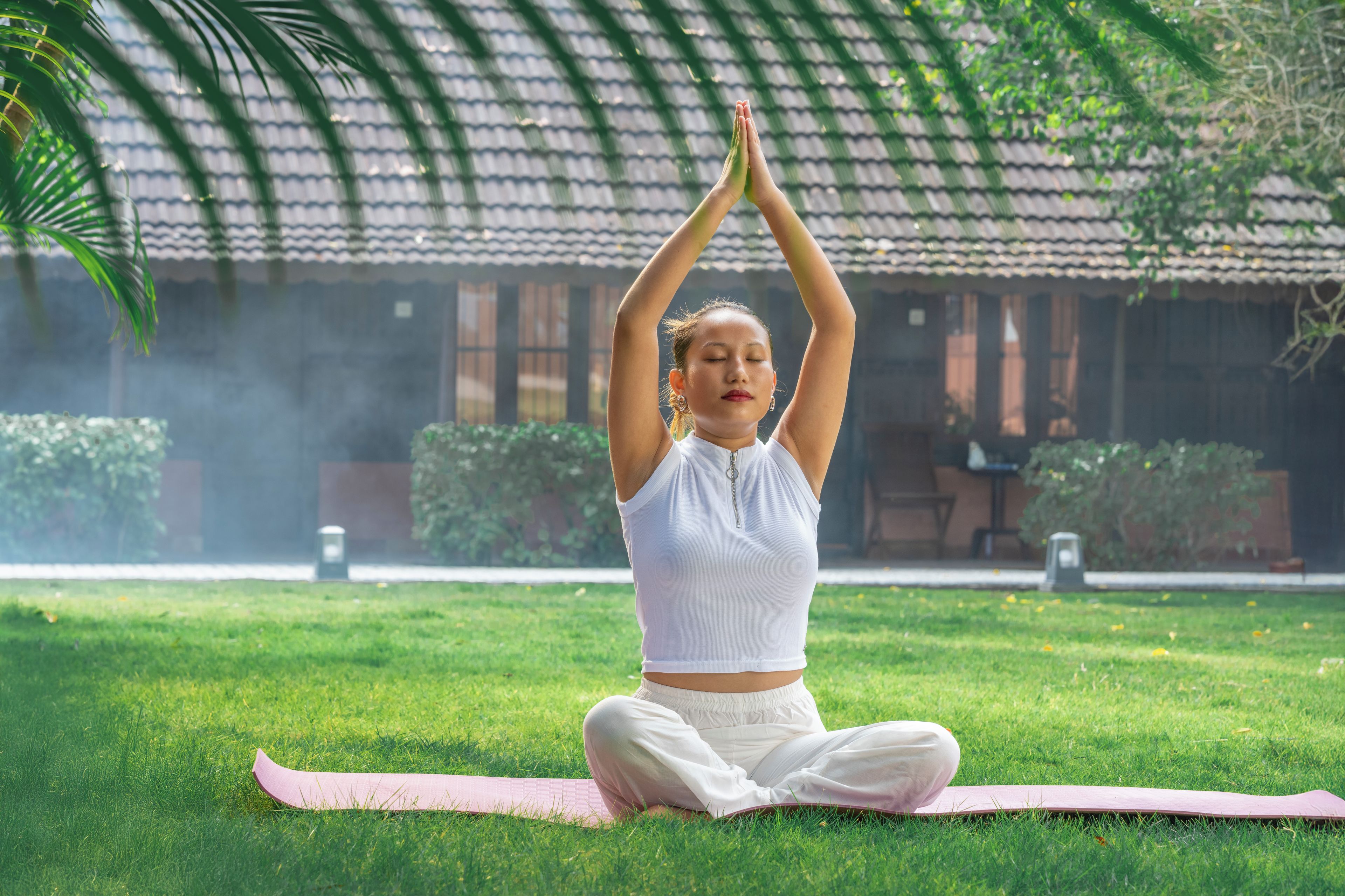 A person sitting on a yoga mat outdoors with a building in the background.