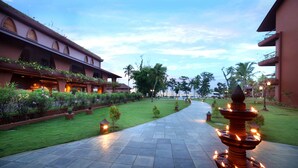 A pathway leading to a building with a garden and a fountain. - Uday Backwater Resort (Ambalapuzha)