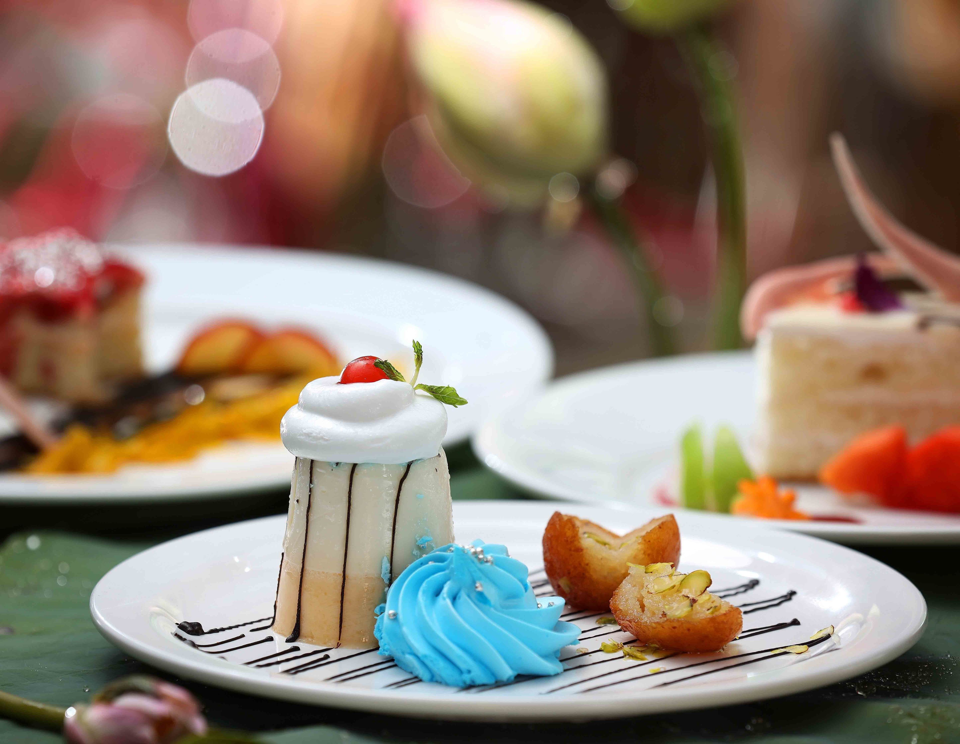 Ein Dessertteller mit verschiedenen Süßigkeiten, darunter ein mehrschichtiger Kuchen, eine Kugel blaue Eiscreme und ein Kuchenstück mit Kirsche.