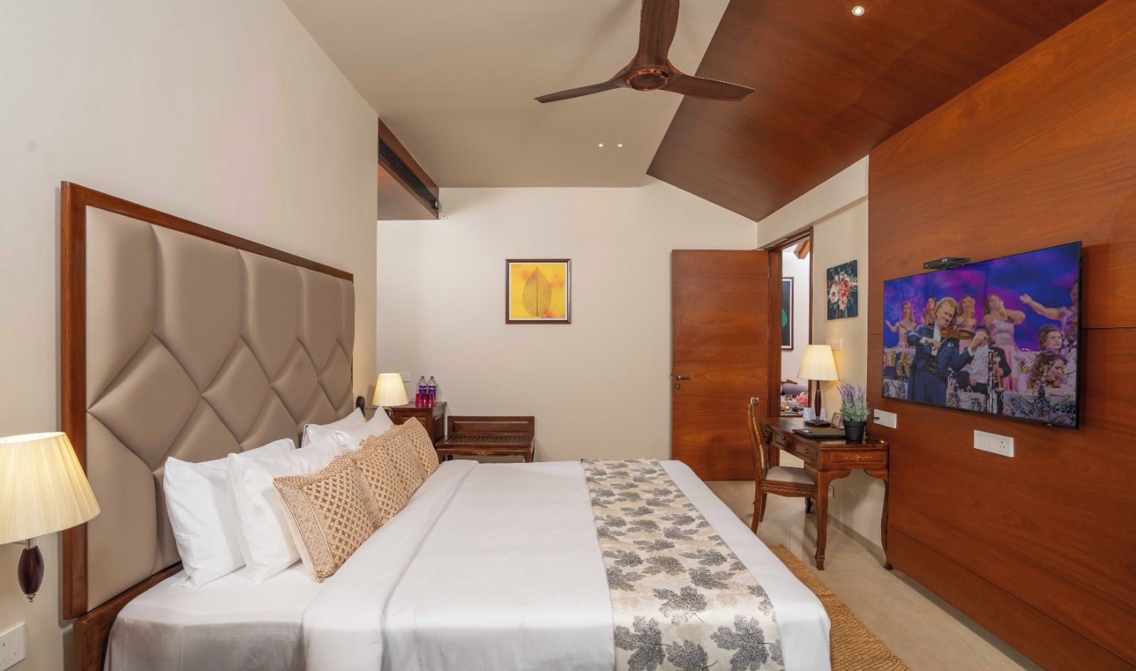 Una habitación de hotel con una cama grande, un escritorio, una silla, un ventilador de techo y obras de arte en las paredes.