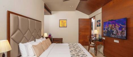 Una habitación de hotel con una cama grande, un escritorio, una silla, un ventilador de techo y obras de arte en las paredes.