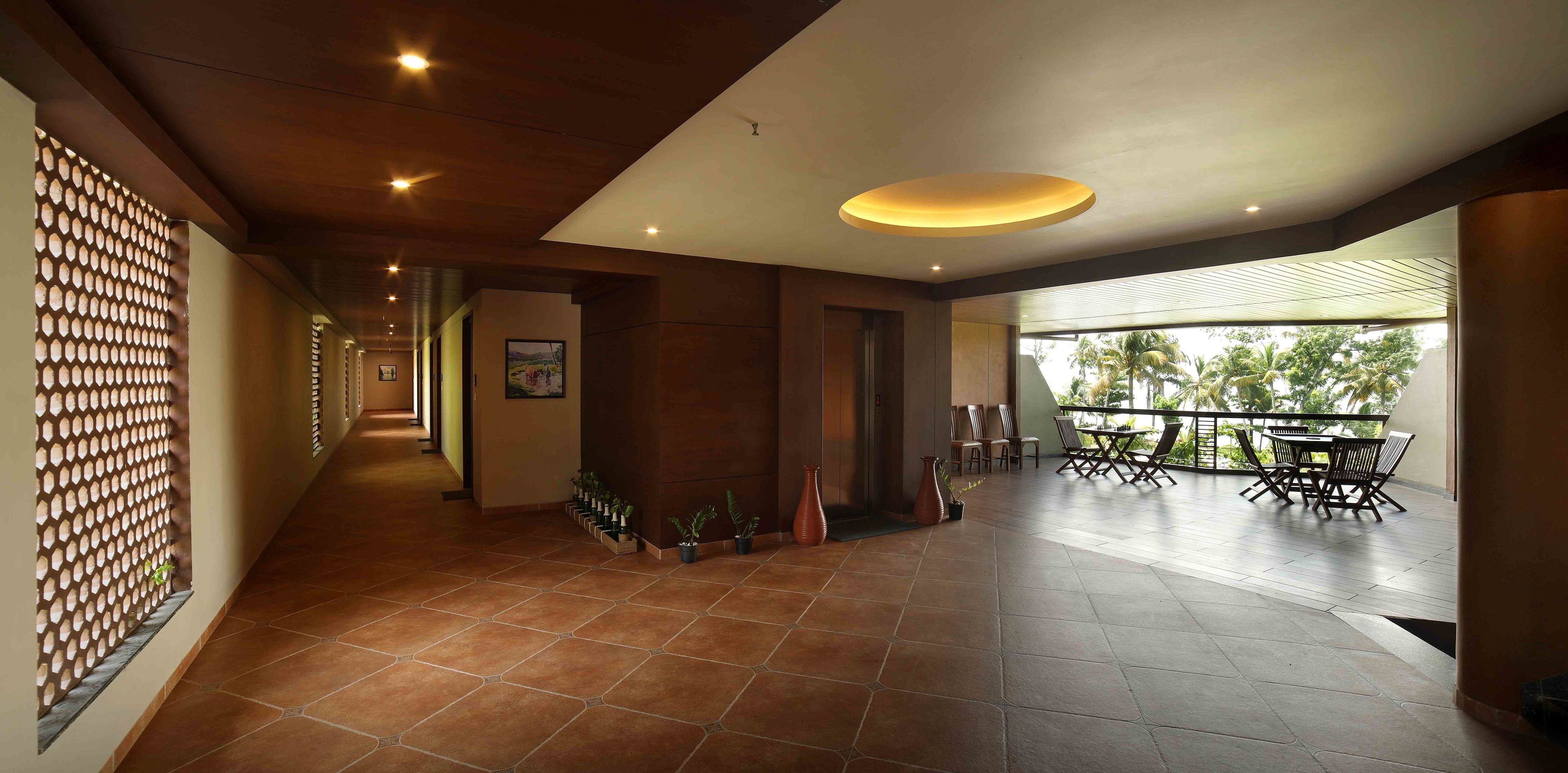 A spacious indoor area with a tiled floor, a reception desk, potted plants, and a balcony with outdoor seating.