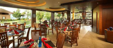 Un restaurante con mesas y sillas de madera, vistas a zonas verdes en el exterior y un diseño de techo moderno.