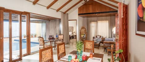 A spacious dining area with wooden furniture, a large table set for a meal, and a view of a swimming pool.