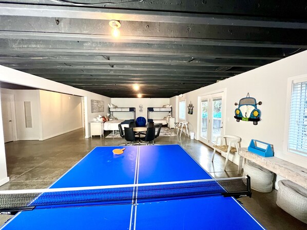 A room with a ping pong table, a bunk bed, and a desk with a chair.