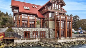 A large, multi-story building with a stone facade and wooden balconies, located near a body of water. - Waterfront - Black Rock Landing (Ucluelet)