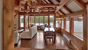 A spacious room with a wooden ceiling, large windows, a dining table, and a sofa. - Waterfront - Black Rock Landing (Ucluelet)