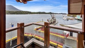A view from a balcony overlooking a dock with boats, a pier, and a forested mountain in the background. - Waterfront - Black Rock Landing (Ucluelet)